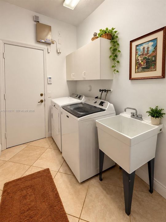 Laundry area featuring tile flooring, white built-in wall cabinetry, and a deep basin utility sink with a dual-handle faucet
