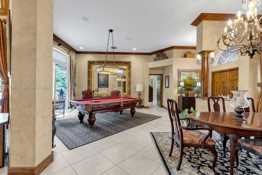 Expansive living area featuring custom crown molding, textured wall finishes, arched architectural detailing, a decorative wood column, and an ornate wrought-iron chandelier