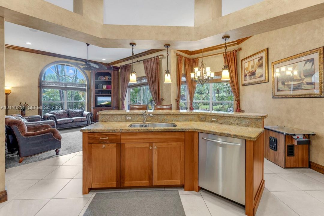 Kitchen island with stone-surface countertop, double-basin stainless steel sink, wood cabinetry, stainless steel dishwasher, and vaulted ceiling