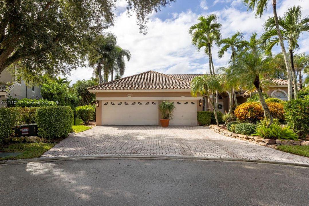 Exterior featuring a two-car garage, tiled roof, paved driveway, and mature landscaping