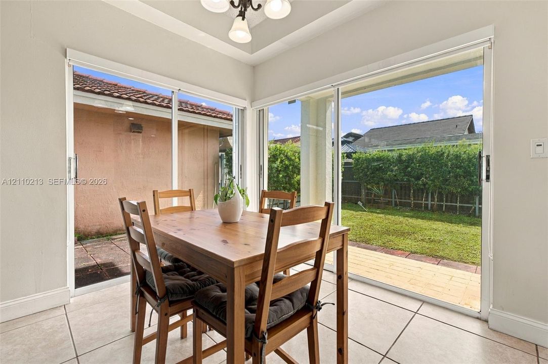 Large tile flooring, tray ceiling with recessed lighting, and expansive dual sliding glass doors opening to a fenced backyard featuring a paved patio