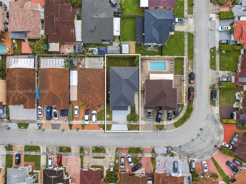 Aerial perspective of a property featuring a multi-pitched dark metal roof and a paved front driveway