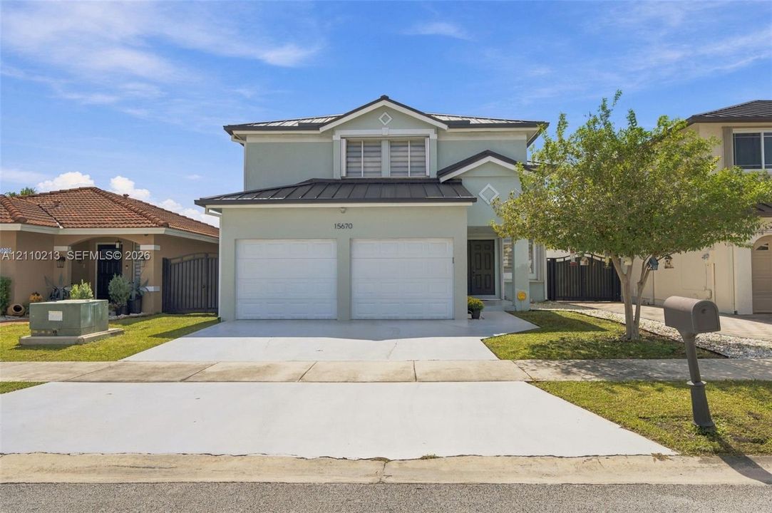 Two-story residence featuring a light-toned stucco exterior, a metal roof, an attached two-car garage, and a paved driveway