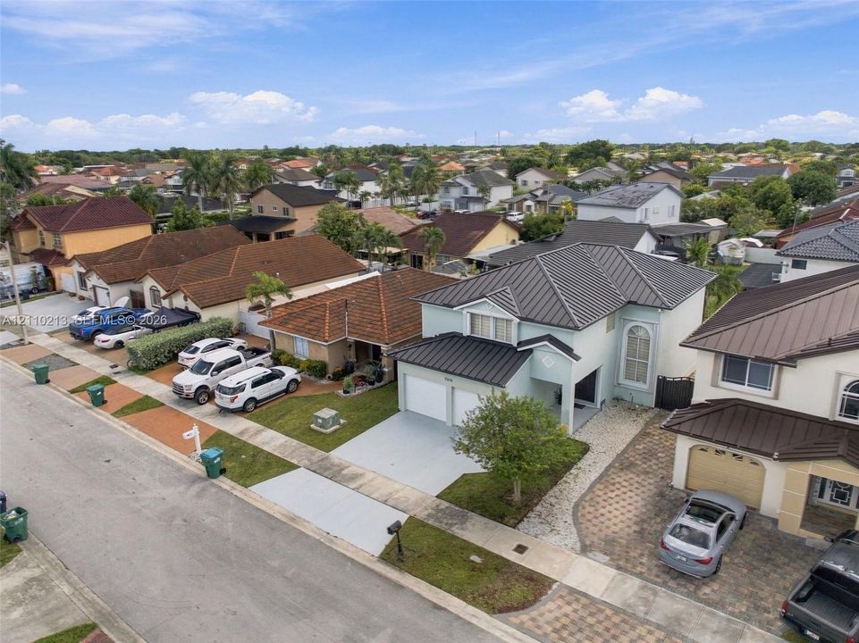 Two-story residence featuring a metal roof, light-colored stucco exterior, attached two-car garage, and a paver driveway