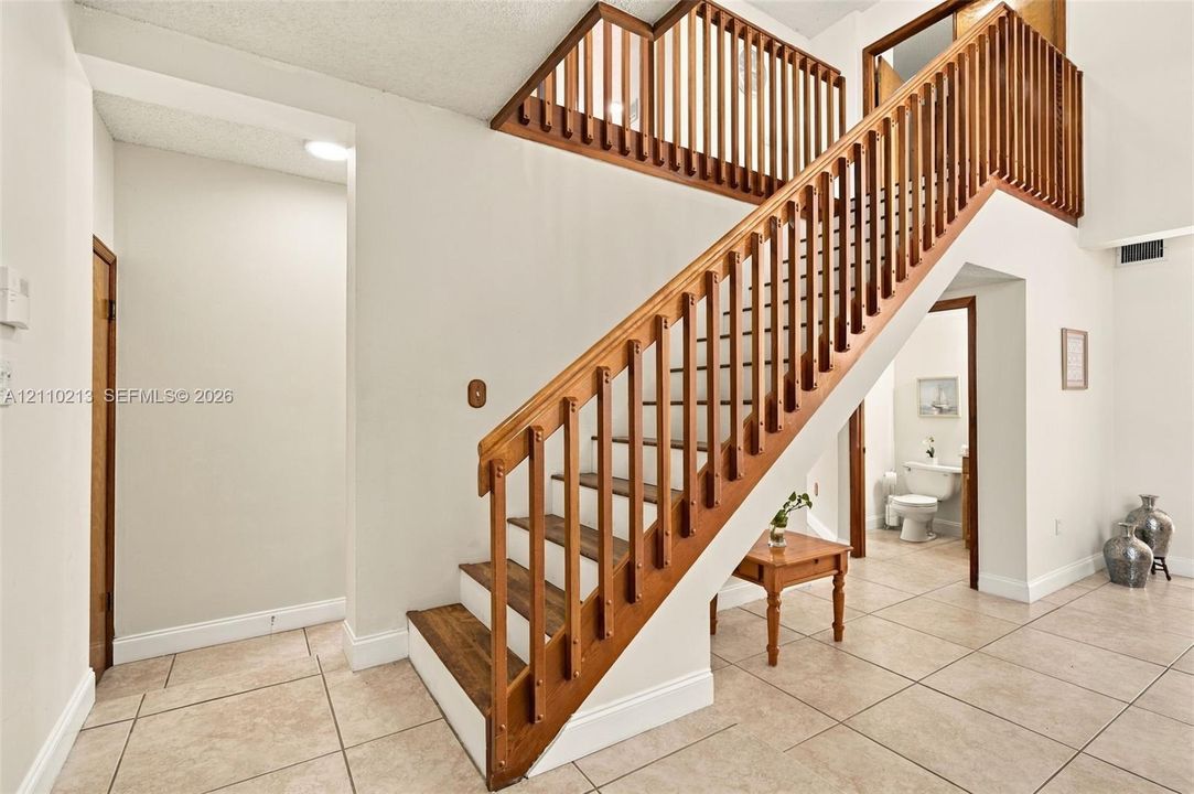 Foyer featuring large-format ceramic tile flooring and an open-riser staircase with a stained-wood railing