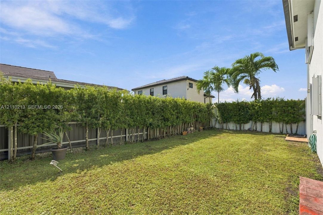 Private backyard featuring a grass lawn, perimeter hedges, and vertical fencing