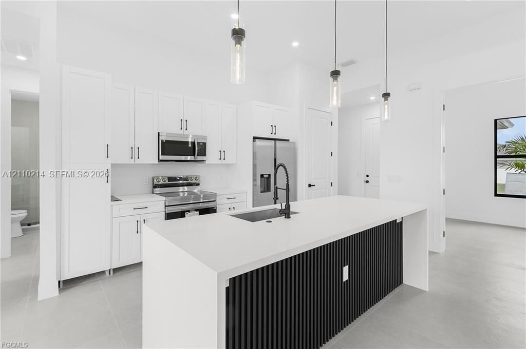 Kitchen featuring white cabinetry, quartz countertops, a black slatted-detail island with an undermount sink, matte black faucet, and three glass pendant lights
