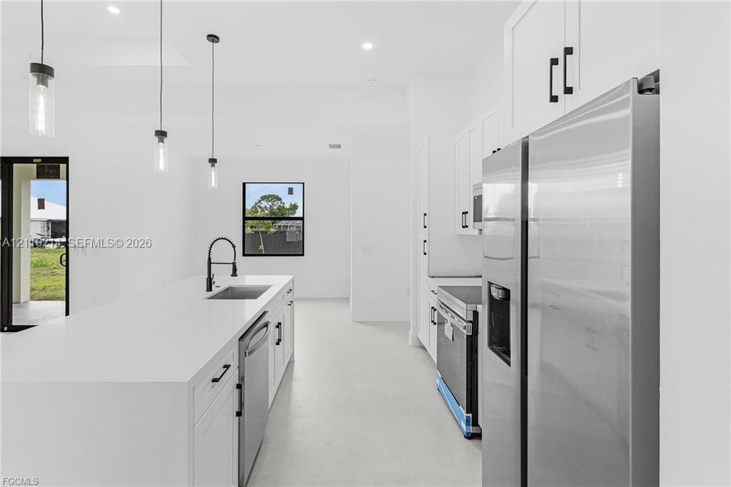 Kitchen featuring a central island with a solid surface countertop, stainless steel appliances, white cabinetry with matte black hardware, and pendant lighting
