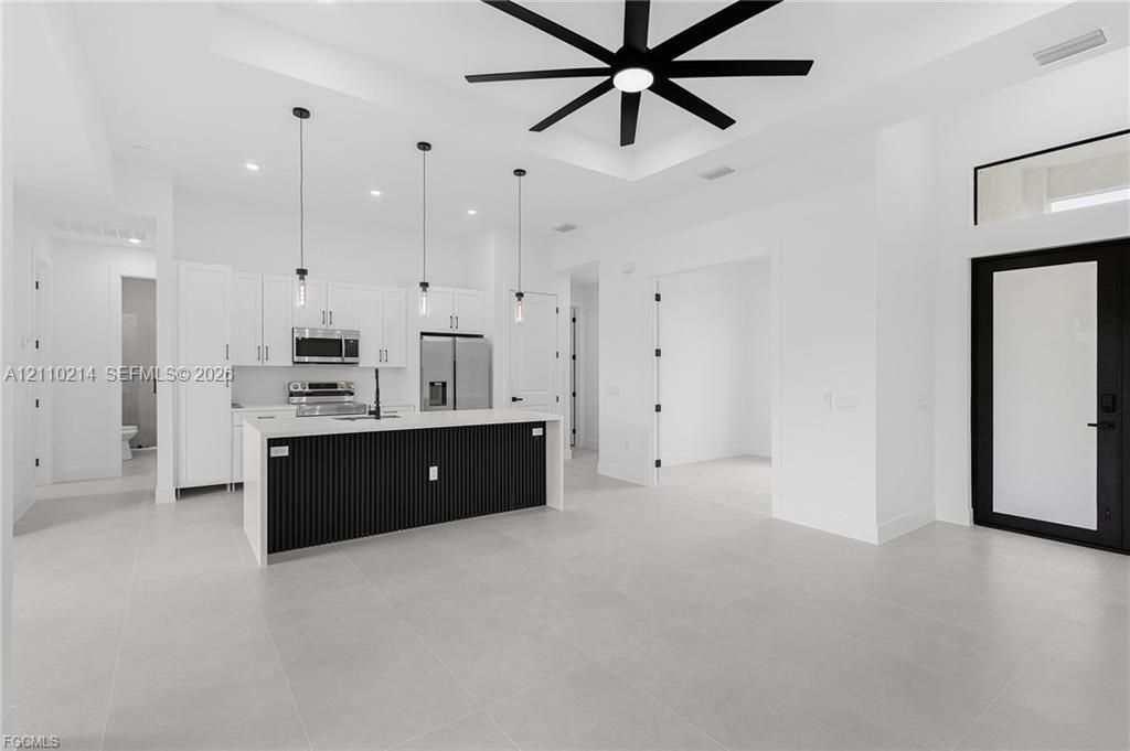 Kitchen featuring a center island with slat detailing and a solid-surface countertop, white cabinetry, integrated stainless steel appliances, large-format tile flooring, and a coffered ceiling with a multi-blade ceiling fan