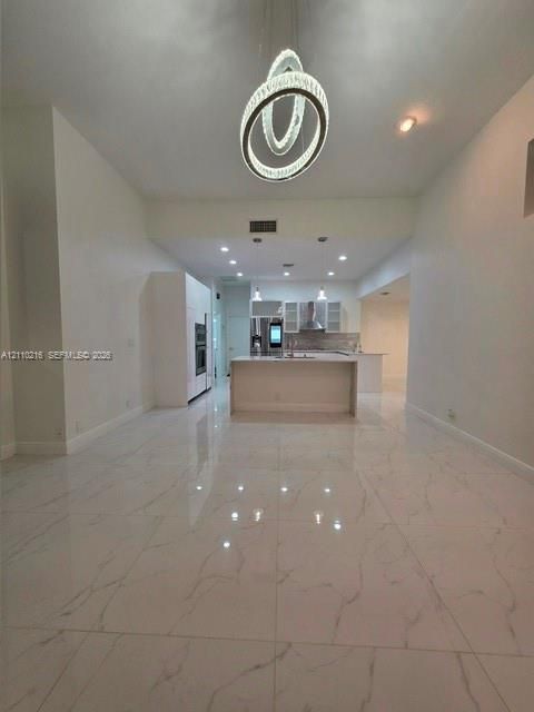 Large-format porcelain tile flooring with veining detail, central island with waterfall edge, recessed ceiling lighting, and sculptural multi-ring pendant fixture