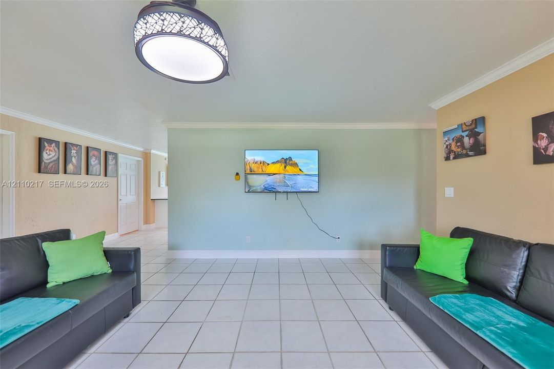Neutral-toned room featuring large-format square tile flooring, crown molding, and a decorative semi-flush mount ceiling fixture with a patterned shade