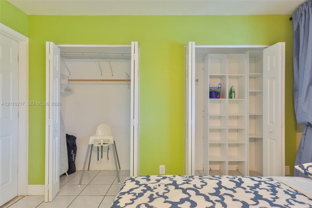 Dual closets featuring bi-fold doors, white interior shelving, and overhead rods, finished with tile flooring