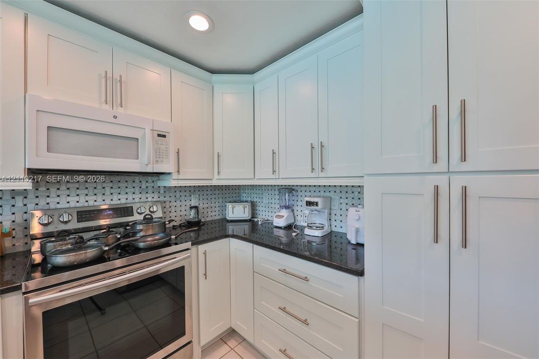 Kitchen featuring white shaker-style cabinetry, dark stone countertops, stainless steel appliances, and a geometric tile backsplash