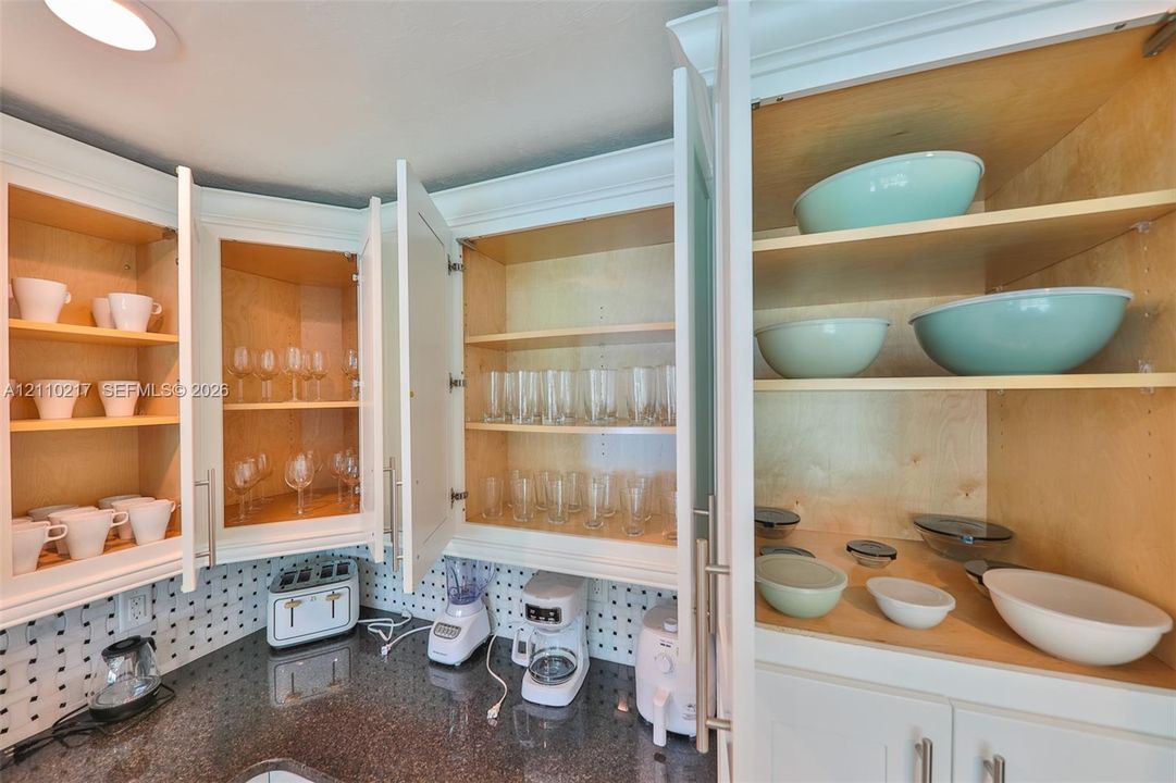 White shaker-style cabinetry with interior shelving, polished stone countertops, and integrated pegboard wall backing