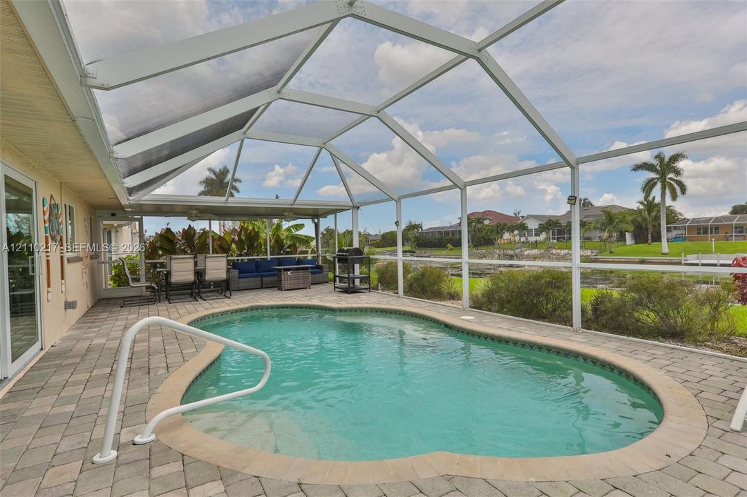 Screened-in patio area featuring a paver deck, inground swimming pool with a metal handrail, and a covered lanai