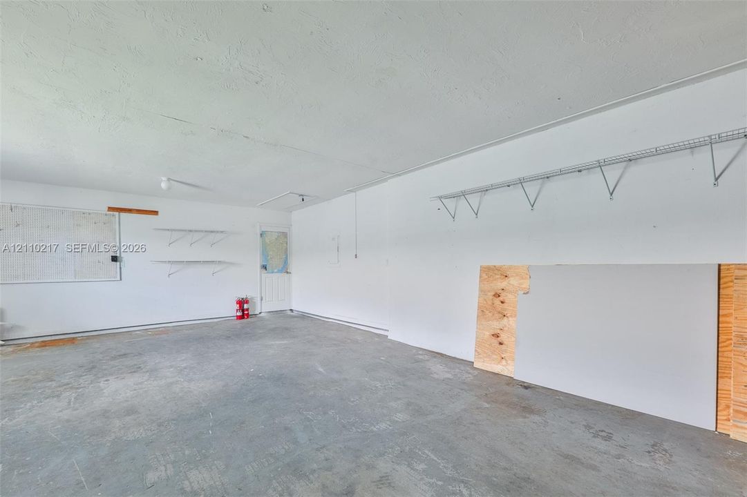 Garage interior featuring finished walls, concrete flooring, and installed wire shelving units