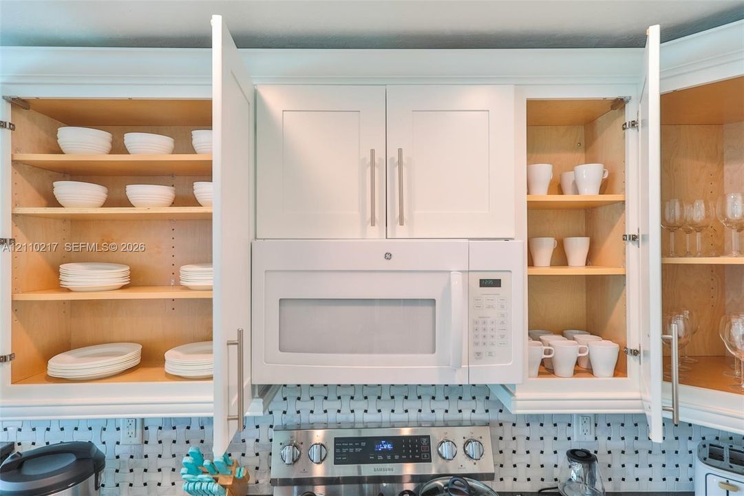 Shaker-style white cabinetry with adjustable shelving and brushed nickel hardware, featuring a built-in over-the-range microwave and a patterned geometric backsplash