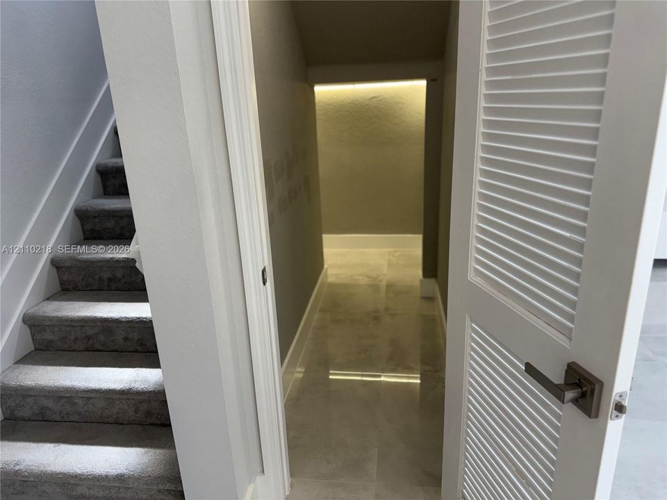 Staircase featuring carpeted steps and a white railing, providing entry to an under-stair storage area with large-format tile flooring, a louvered door, and recessed linear lighting