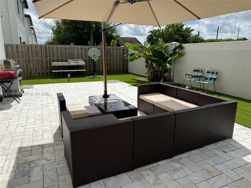 Outdoor space featuring a paved patio, synthetic turf lawn, perimeter wood fencing, and masonry privacy wall