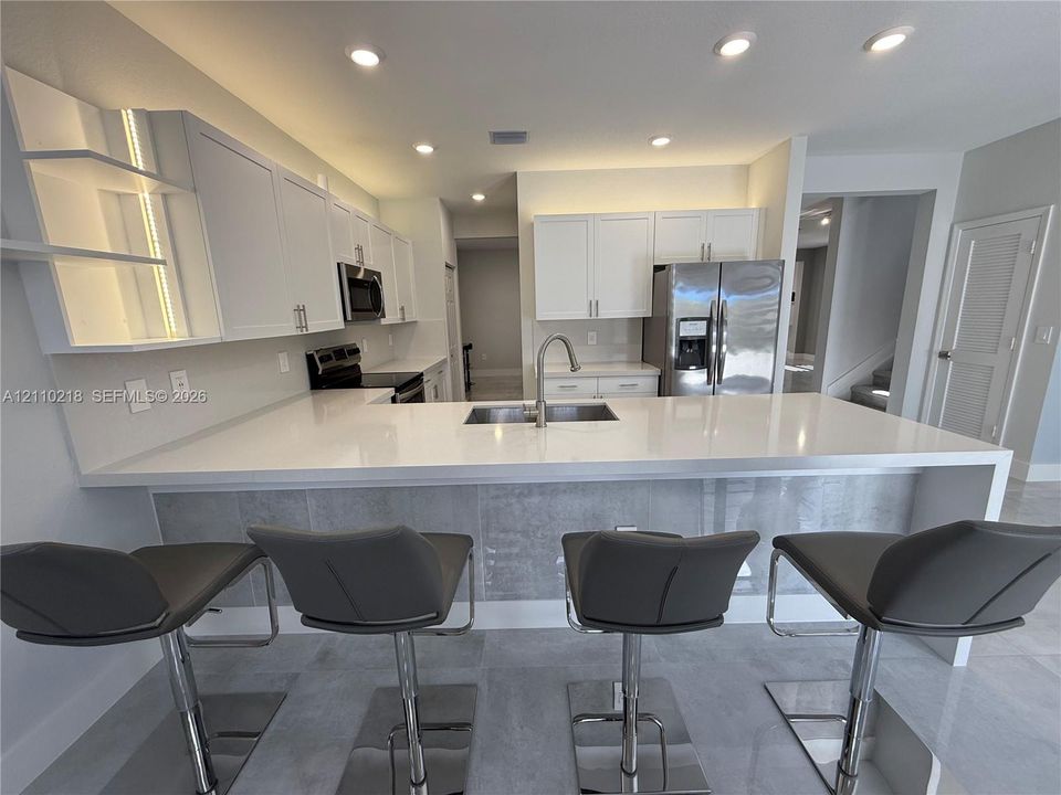 Kitchen featuring white shaker-style cabinetry, quartz countertops, an expansive breakfast bar with a tile-faced base, stainless steel appliances, and recessed ceiling lighting