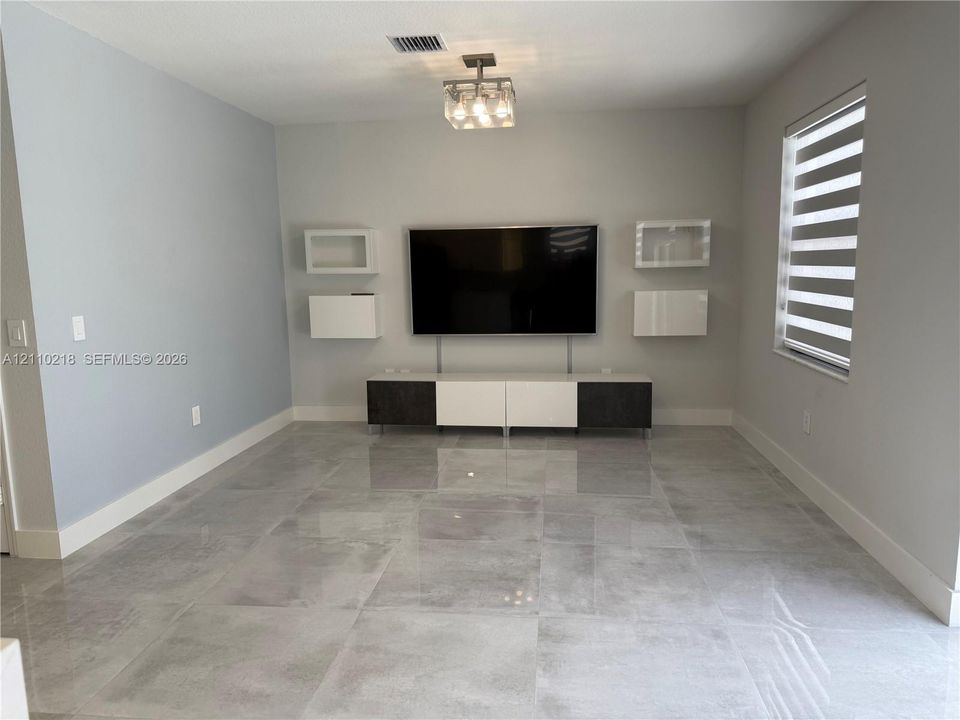 Large-format polished tile flooring, built-in dual-tone media cabinetry with floating wall units, and modern square-cased light fixture