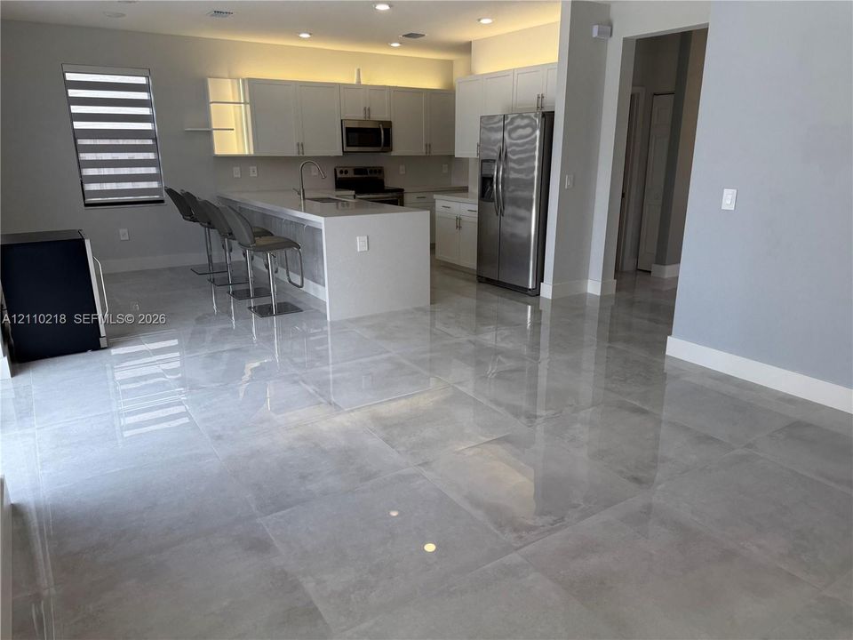 Kitchen featuring high-gloss cabinetry, stone-surface waterfall island with an integrated sink, polished large-format tile flooring, stainless steel appliances, and recessed ceiling lighting