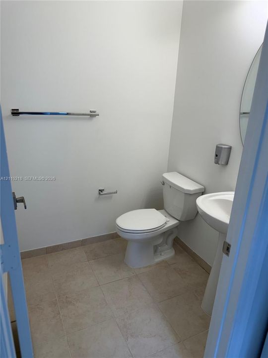 Neutral-toned tile flooring, pedestal sink, oval wall-mounted mirror, and chrome hardware throughout