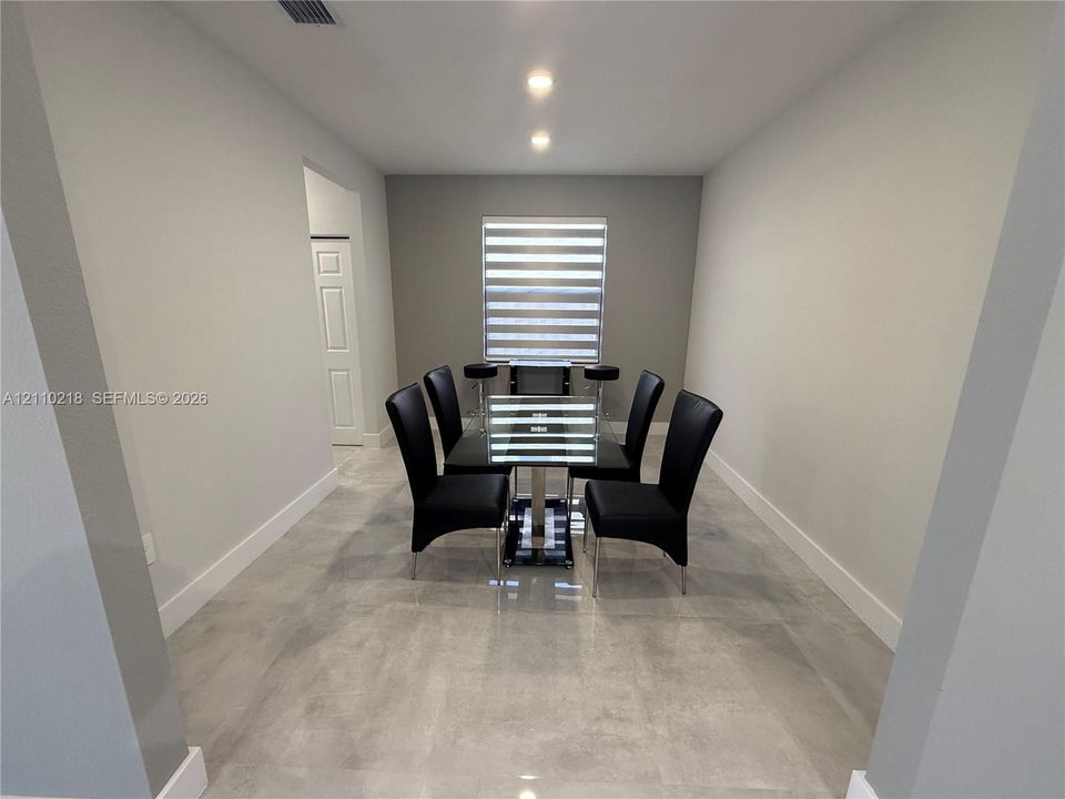 Neutral-toned interior featuring large-format stone-finish tile flooring, recessed ceiling lighting, and a single window with horizontal light-filtering shades