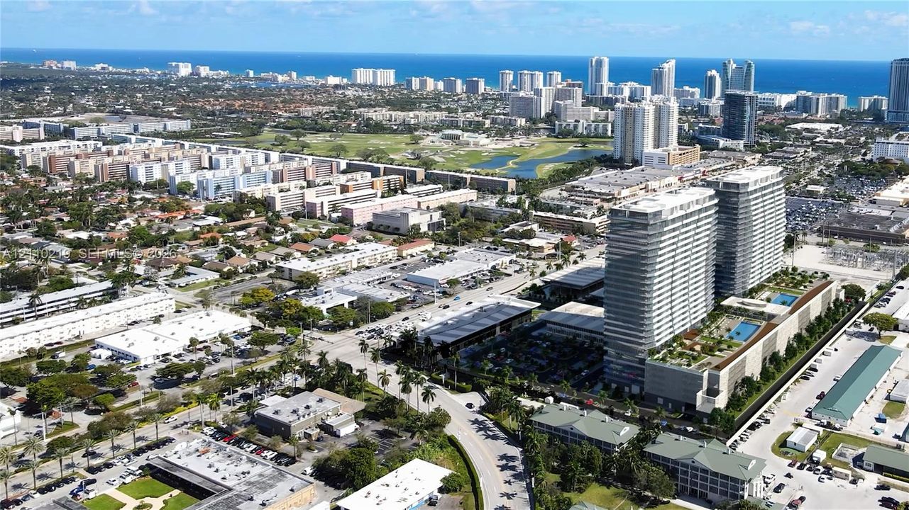 Aerial perspective of high-rise towers featuring a multi-level parking structure, landscaped rooftop deck, and swimming pools