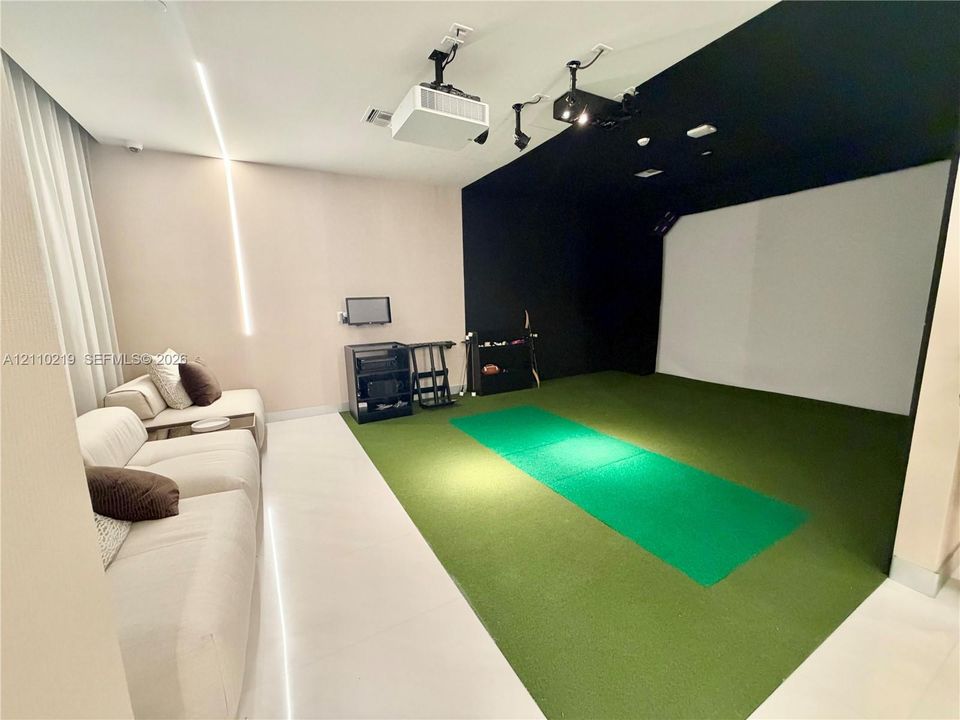 Dedicated room featuring a built-in golf simulator system, projection equipment, synthetic turf flooring, and recessed ceiling lighting