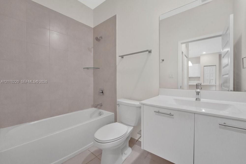 Bathroom featuring a vanity with integrated sink, large wall-mounted mirror, tub-shower combination with floor-to-ceiling tile surround, and brushed metal hardware
