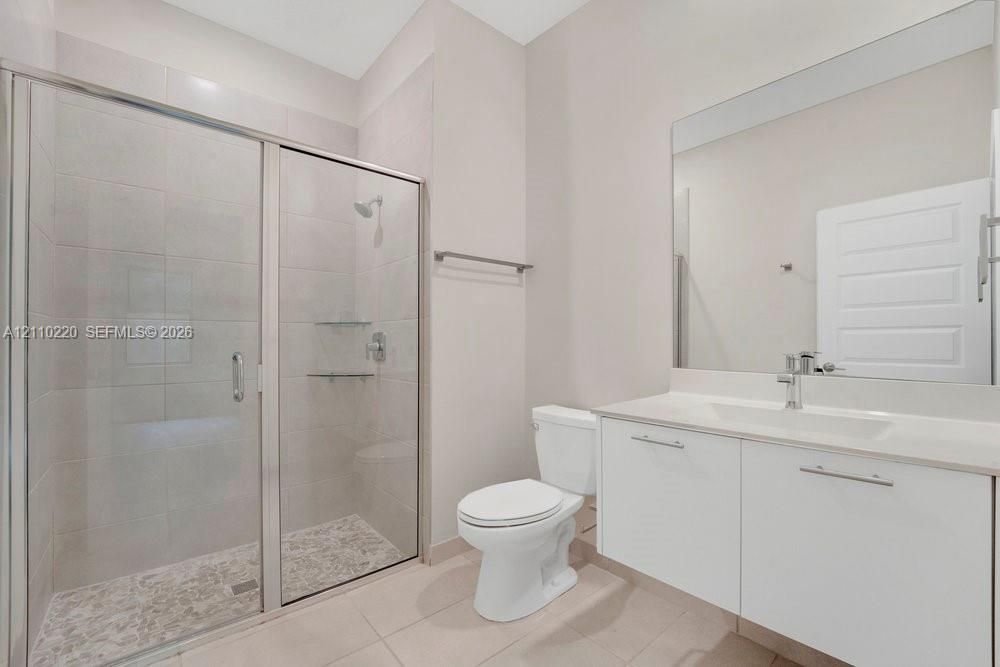 Bathroom featuring a glass-enclosed shower with tiled walls and flooring, a wall-to-wall vanity with an integrated sink, a large vanity mirror, and a chrome-finish faucet