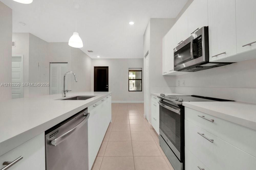 Kitchen featuring white flat-panel cabinetry, light-toned stone countertops, a stainless steel appliance suite, an undermount sink with a gooseneck faucet, and tile flooring