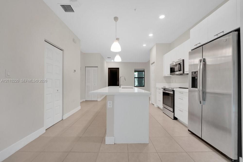Kitchen featuring a central island with a solid-surface countertop, white flat-panel cabinetry, stainless steel appliances, recessed ceiling lighting, and large-format tile flooring