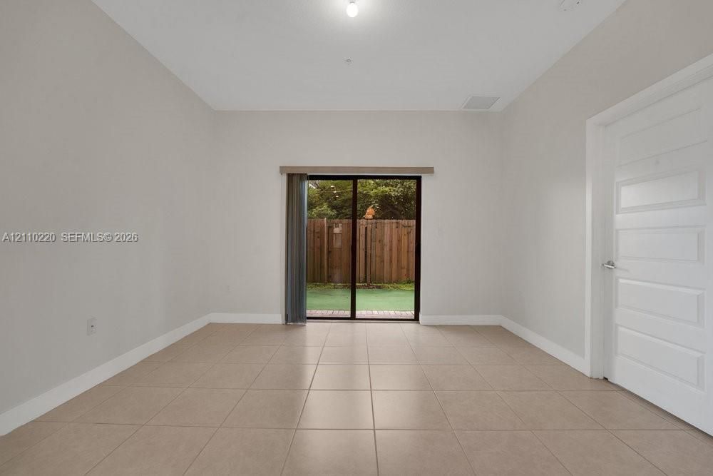 Neutral-toned interior featuring large-format floor tiles, high ceilings, a five-panel interior door, and sliding glass doors with access to an exterior fenced area