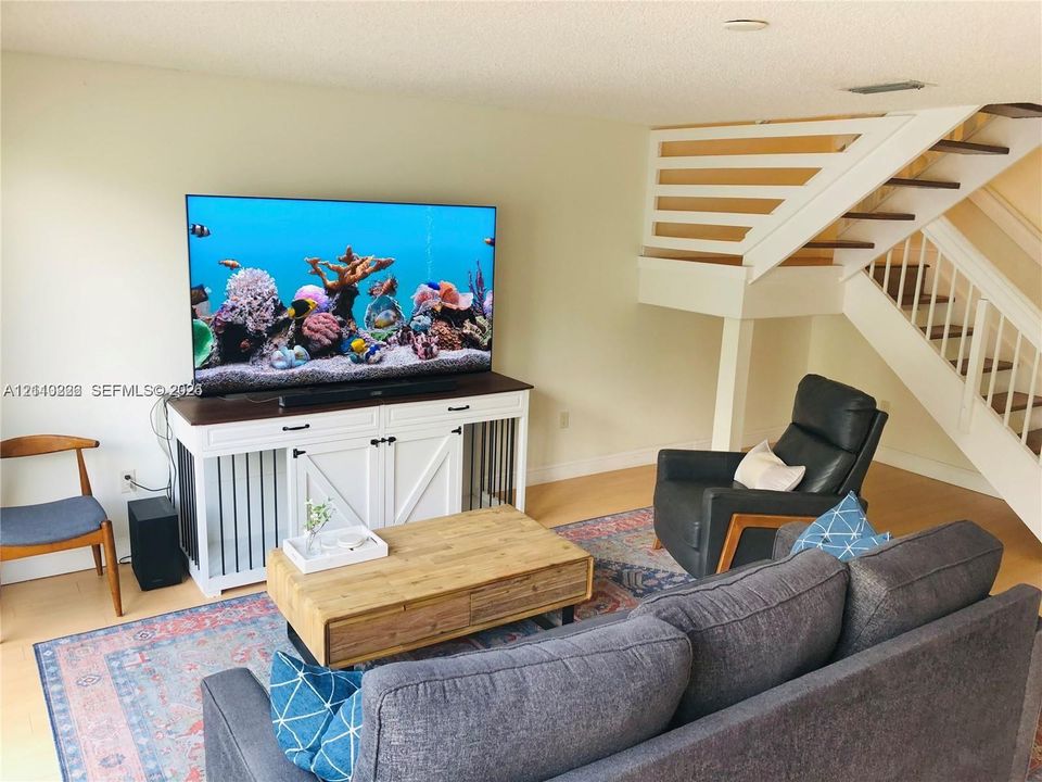 Open-concept living space featuring wood-finish flooring and a staircase with white balusters and wood handrails