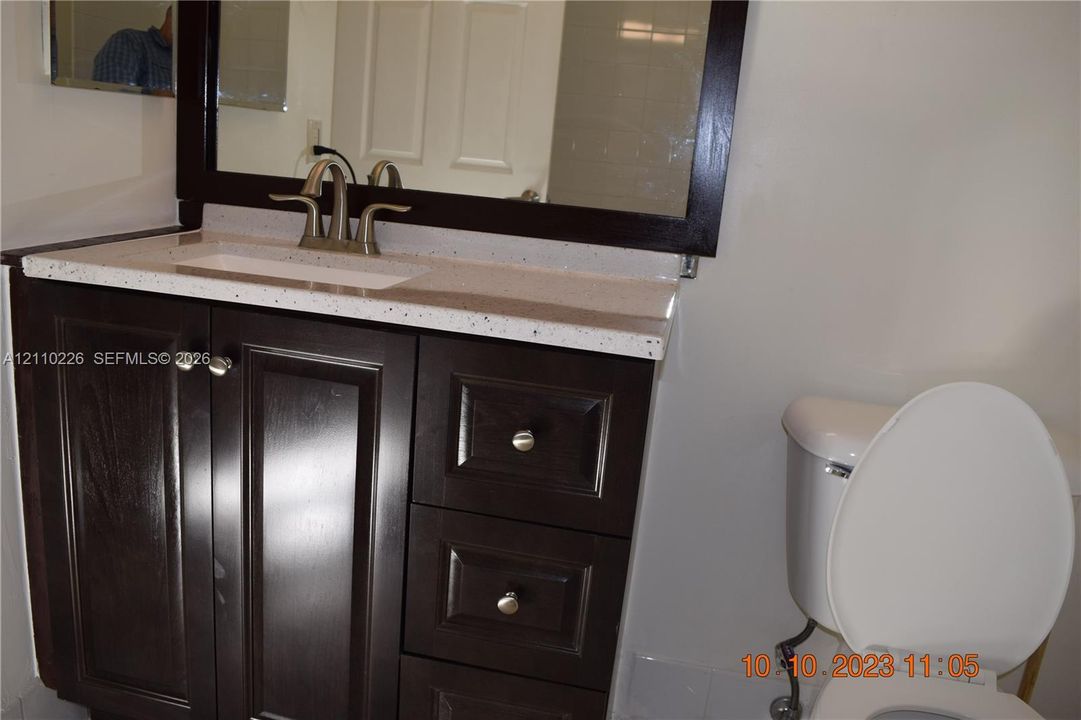 Dark wood vanity featuring a speckled white countertop, rectangular basin, brushed metal faucet, and matching framed mirror
