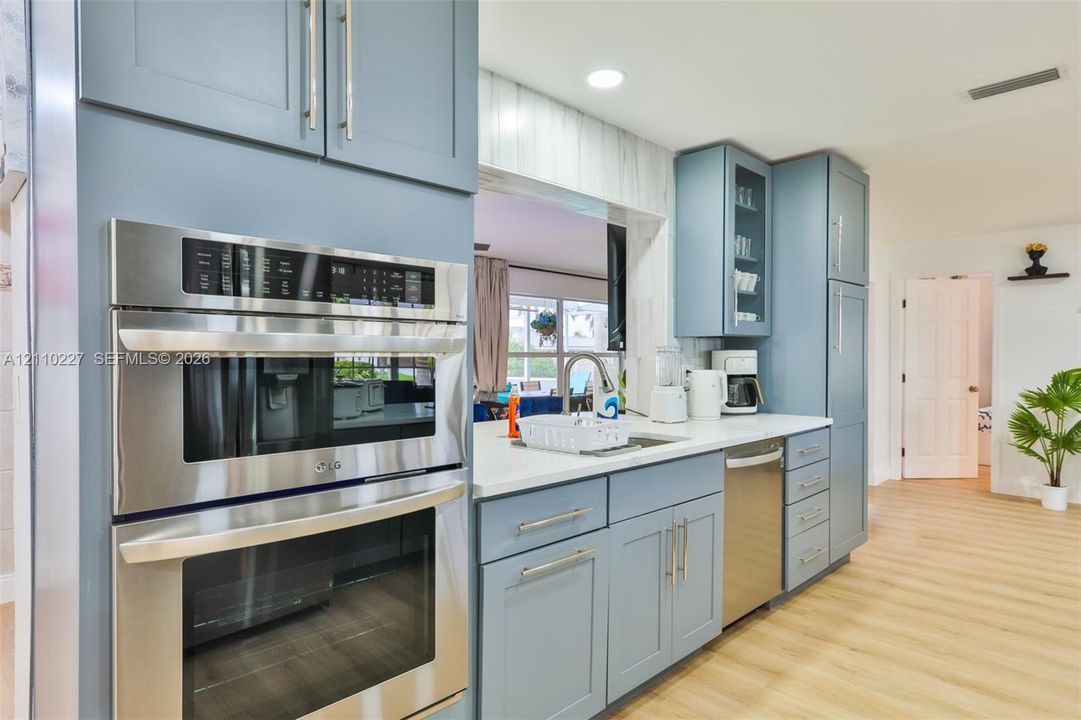 Kitchen featuring blue cabinetry, light-toned countertops, a built-in stainless steel double wall oven, a stainless steel dishwasher, and wood-finish flooring