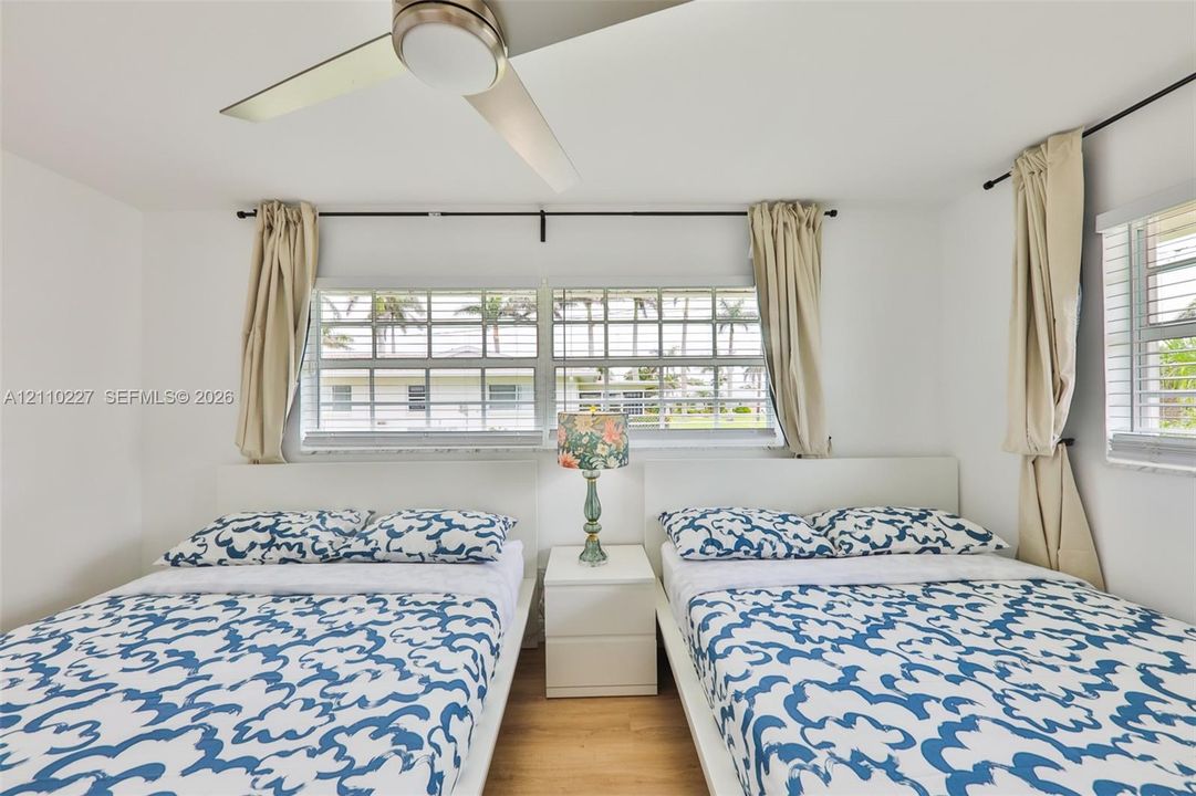Room featuring wood-finish flooring, a contemporary ceiling fan with integrated lighting, and multiple horizontal sliding windows with metal rod hardware