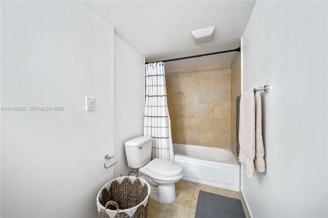 Full bathroom featuring a tub-shower combination with square stone-finish wall tile, a two-piece white toilet, and tile flooring
