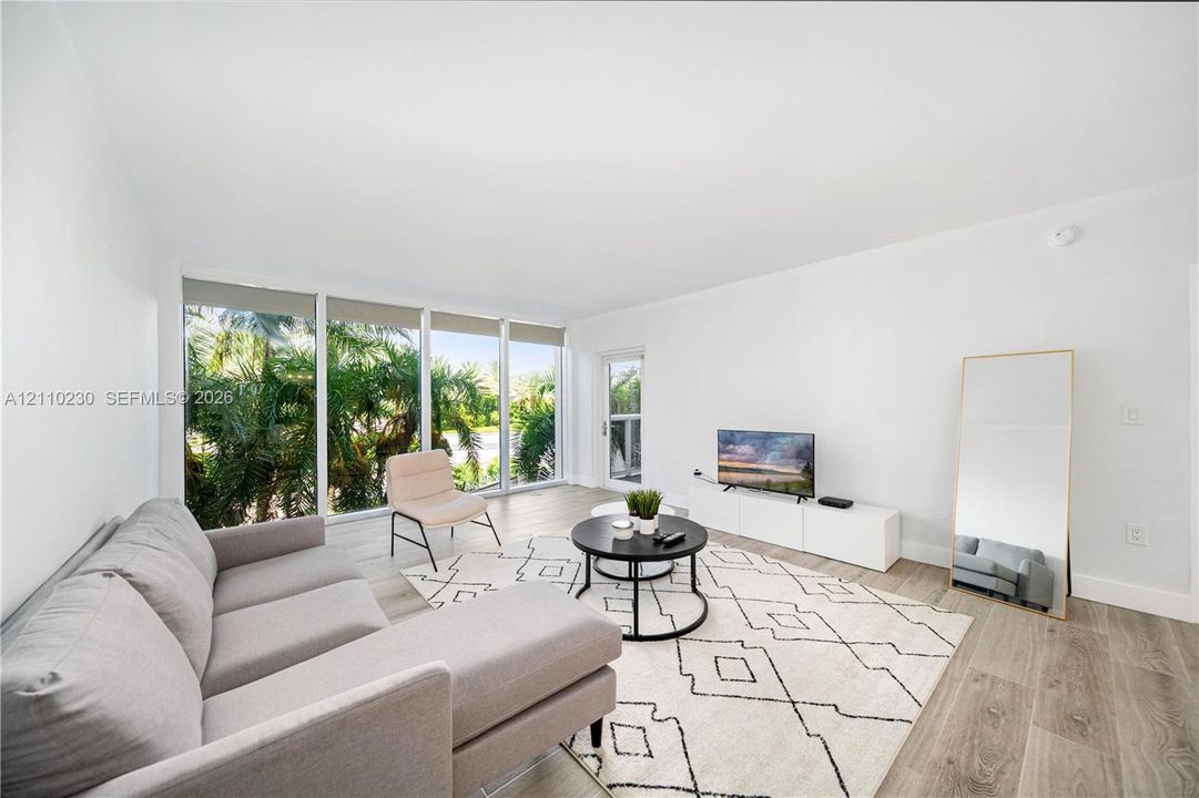 Living area featuring wood-finish flooring, floor-to-ceiling windows, and glass-paneled entry door