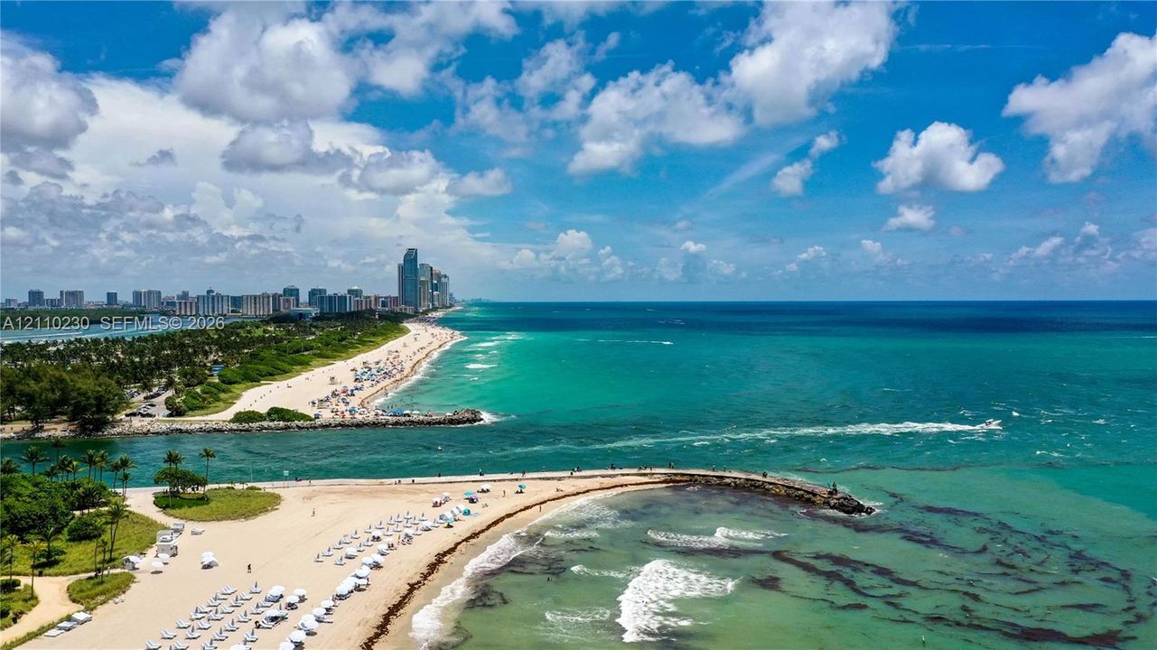 Aerial coastal perspective featuring a direct oceanfront shoreline, sandy beach access, and stone jetty infrastructure