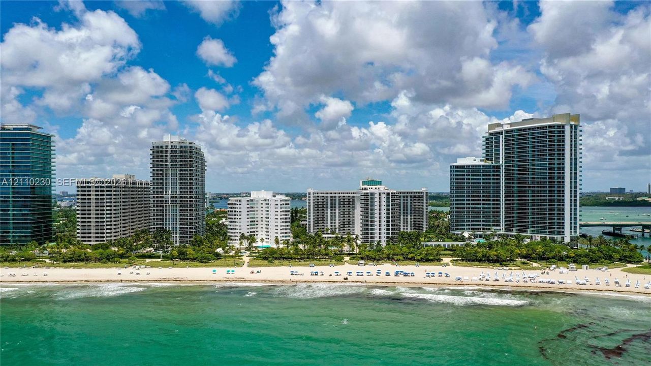 Aerial perspective of coastal high-rise structures featuring direct shoreline access, sandy beachfront, and perimeter landscaping