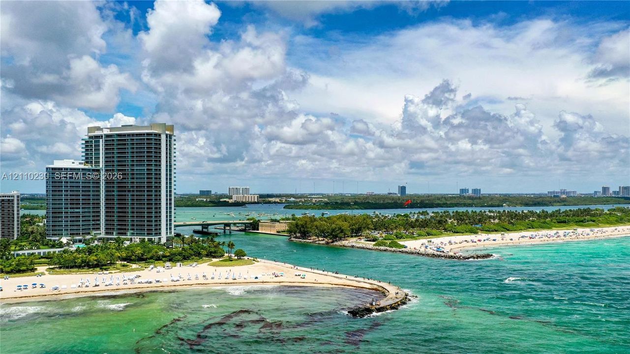 High-rise residential tower featuring a concrete facade, expansive glass windows, direct waterfront access, and proximity to a sand beach and coastal inlet