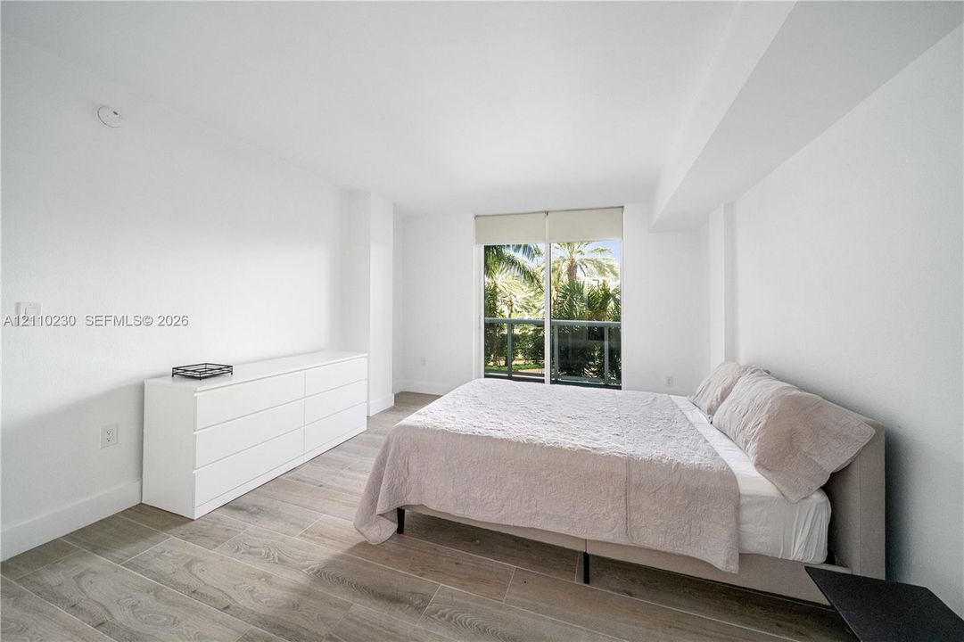 Interior space featuring wood-finish tile flooring, white walls, and floor-to-ceiling glass sliding doors opening to an exterior balcony