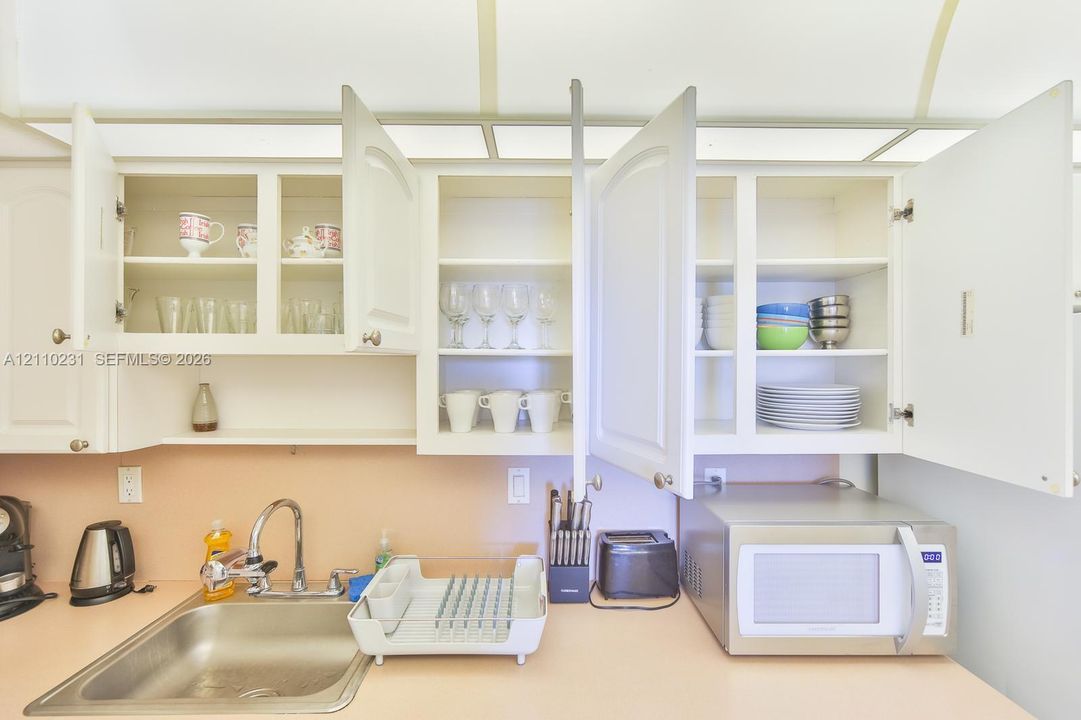 White cabinetry with paneled doors, solid-surface countertop, stainless steel sink, and integrated overhead lighting