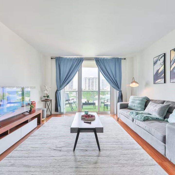 Living area featuring wood-finish flooring, floor-to-ceiling glass sliding doors, and a private balcony