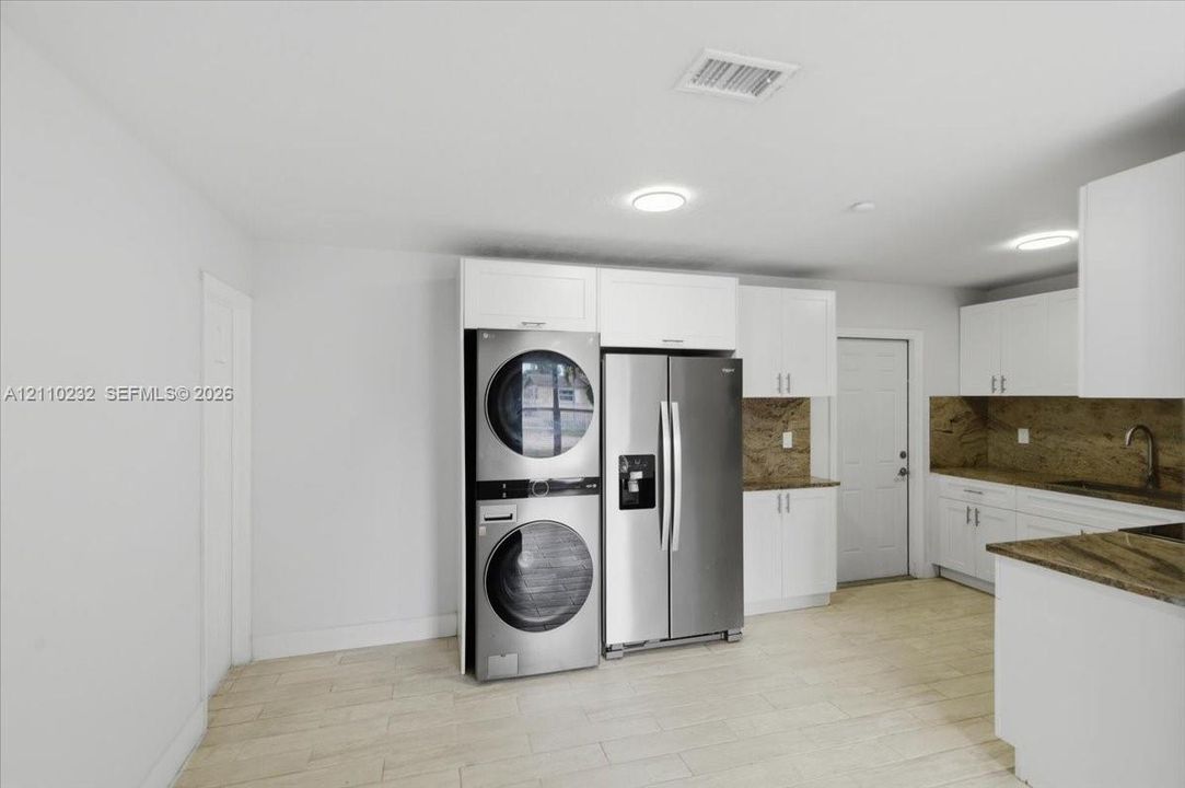 White cabinetry featuring shaker-style doors, stone-finish countertops, stainless steel appliances, and wood-finish flooring
