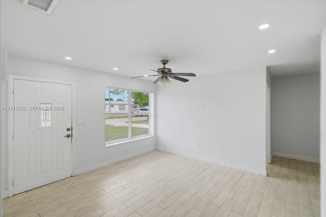 Interior space featuring wood-finish tile flooring, recessed ceiling lighting, a multi-blade ceiling fan, and a six-panel entry door with an integrated glass light