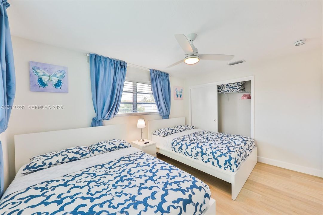 Room featuring wood-finish flooring, a ceiling fan with integrated lighting, horizontal window blinds, and a built-in closet with sliding doors
